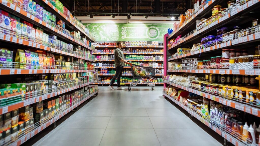 young man with shopping cart between store shelf grocery