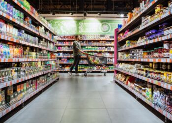 young man with shopping cart between store shelf grocery